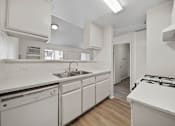 Thumbnail 30 of 38 - A white kitchen with a stove, sink, and cabinets.