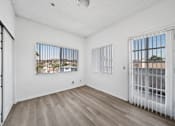 Thumbnail 8 of 14 - A room with white walls and wooden flooring, featuring two windows with metal bars.