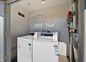 Thumbnail 10 of 14 - A white washing machine is in a small room with a door open.