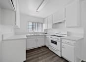 Thumbnail 21 of 33 - A white kitchen with a stove, sink, and cabinets.