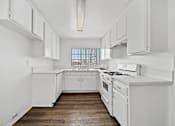 Thumbnail 19 of 33 - A white kitchen with wooden floors and white appliances.