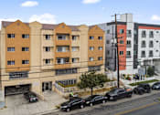 Thumbnail 2 of 33 - A street view of a multi-story building with cars parked in front.