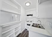 Thumbnail 30 of 30 - A small white kitchen with a sink and a stove.