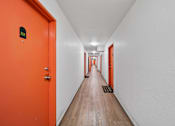 Thumbnail 13 of 29 - A long hallway with orange doors and a white wall.