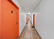 Thumbnail 14 of 29 - A long hallway with orange doors and white walls.