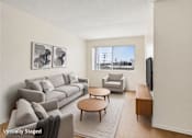 Thumbnail 1 of 21 - A living room with a grey couch, a coffee table, and a television.