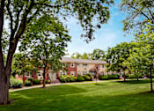 Thumbnail 14 of 22 - A large red brick building with a white door and windows is surrounded by green trees and grass. at Rivercrest Apartments, New Jersey, 08854