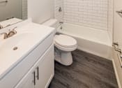 Thumbnail 3 of 11 - Fully renovated bathroom with subway tile, gray plank flooring, and white vanity at Kings Gate West Apartments, Camillus, NY, 13031