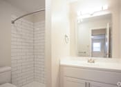 Thumbnail 5 of 11 - A white bathroom with a white toilet, a white sink, and a white tiled shower at Kings Gate West Apartments, New York