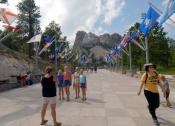 Thumbnail 6 of 20 - a group of people walking on a bridge with flags and mountains in the background  at Antelope Ridge, Box Elder, SD