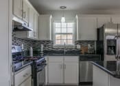 Thumbnail 24 of 31 - a kitchen with white cabinets and black countertops and splash guards at Village of Cottonwood Springs