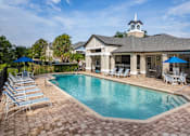 Thumbnail 1 of 48 - A pool surrounded by chairs and umbrellas in front of a house.
