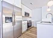 Thumbnail 1 of 9 - A modern kitchen with a stainless steel refrigerator and white cabinets.