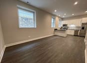 Thumbnail 1 of 20 - A spacious kitchen and living room with wood flooring and white cabinetry.