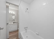 Thumbnail 21 of 37 - A white bathroom with a tub and a mirror.