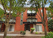 Thumbnail 19 of 31 - A red brick building with a balcony and a black door.