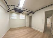 Thumbnail 17 of 17 - A room with wooden flooring and white walls, equipped with a pull-down attic ladder.