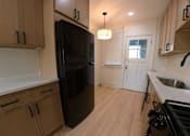 Thumbnail 2 of 13 - A kitchen with a black fridge and wooden cabinets.