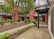 Thumbnail 29 of 31 - A brick building with a patio and bushes in front.
