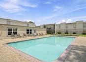 Thumbnail 2 of 37 - A swimming pool in front of a building with a clear blue sky.