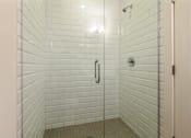 Thumbnail 7 of 13 - A white tiled shower with a glass door.