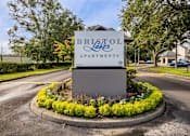 Thumbnail 6 of 48 - A sign for Bristol Lakes Apartments is surrounded by flowers and greenery.