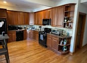 Thumbnail 6 of 13 - A kitchen with wooden cabinets and black appliances.