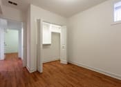 Thumbnail 8 of 13 - A room with white walls and wood flooring with a doorway open to another room.