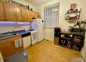 Thumbnail 14 of 25 - A small kitchen with wooden cabinets and a white refrigerator.