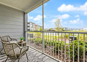 Thumbnail 24 of 37 - A balcony with a chair and table overlooking a green area.