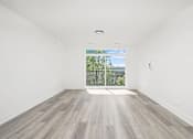 Thumbnail 9 of 27 - A room with a wooden floor and a view of a fence and trees outside.