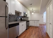 Thumbnail 1 of 13 - A kitchen with white cabinets and a wooden floor.