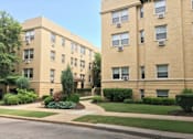 Thumbnail 2 of 17 - A beige apartment building with green bushes in front.