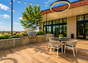 Thumbnail 8 of 18 - A patio with a table and chairs is set up outside a building.