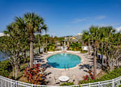 Thumbnail 5 of 37 - A pool surrounded by palm trees and a white fence.