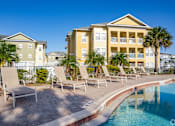 Thumbnail 16 of 37 - A pool area with chairs and a building in the background.