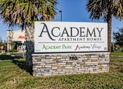 Thumbnail 17 of 37 - A stone sign for Academy Park Apartment Homes stands in front of a palm tree.