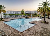 Thumbnail 28 of 37 - A large outdoor swimming pool surrounded by palm trees and lounge chairs.