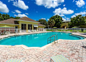 Thumbnail 15 of 29 - A swimming pool surrounded by a brick patio and a yellow building in the background.