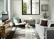 Thumbnail 5 of 31 - A modern living room with a grey couch, a wooden cabinet, and a large window.
