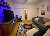 Thumbnail 11 of 25 - A living room with a grey couch and a wooden coffee table.