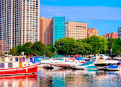 Thumbnail 16 of 16 - A red boat is docked in a marina with other boats and buildings in the background.