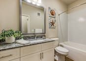 Thumbnail 15 of 46 - A bathroom with a white toilet, a sink, a mirror, and a bathtub.