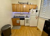 Thumbnail 4 of 25 - A small kitchen with a white fridge and wooden cabinets.