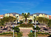 Thumbnail 24 of 44 - A large building with a yellowish hue is surrounded by trees and a fountain in the middle of a plaza.