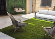 Thumbnail 13 of 16 - A patio with a white couch, a green rug, and a chair.