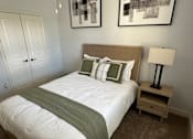 Thumbnail 5 of 29 - A bed with a green blanket and pillows is in the foreground with a lamp and two pictures on the wall.