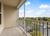Thumbnail 20 of 50 - A balcony with a view of a parking lot and trees.