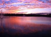 Thumbnail 10 of 44 - A beautiful sunset over a lake with a fountain in the foreground.