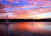 Thumbnail 11 of 44 - A fountain in the middle of a lake with a beautiful sunset in the background.